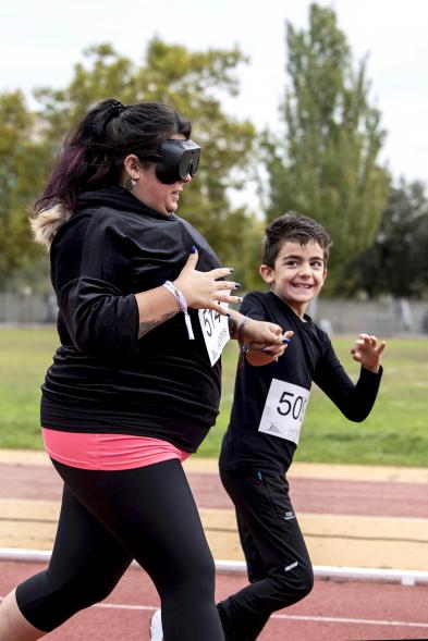 Mujer corre con gafas cegadoras ayudada por un joven guía