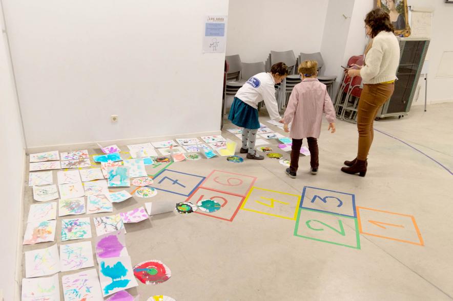 Pinturas infantiles en el suelo mientras niños las van colocando
